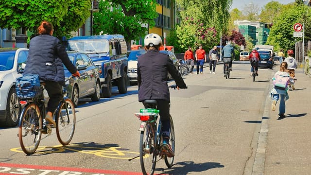 People cycling on a city street with cars.