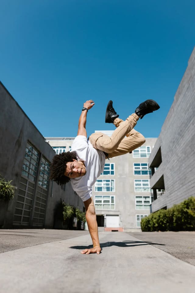 Danseur de rue en appui sur une main, figure acrobatique devant un immeuble.