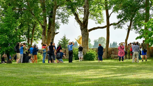 People watching a yellow object in a green park.