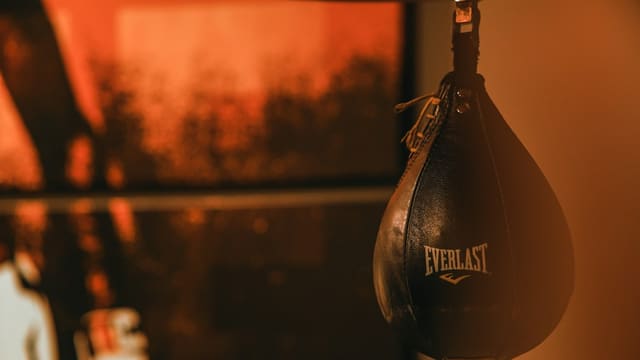 Une poire de vitesse en cuir noir suspendue dans une salle de boxe, éclairée par une lumière orangée.