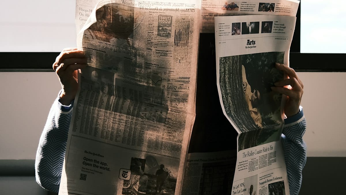 Une personne lisant un journal papier déployé devant elle