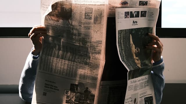 Une personne lisant un journal papier déployé devant elle