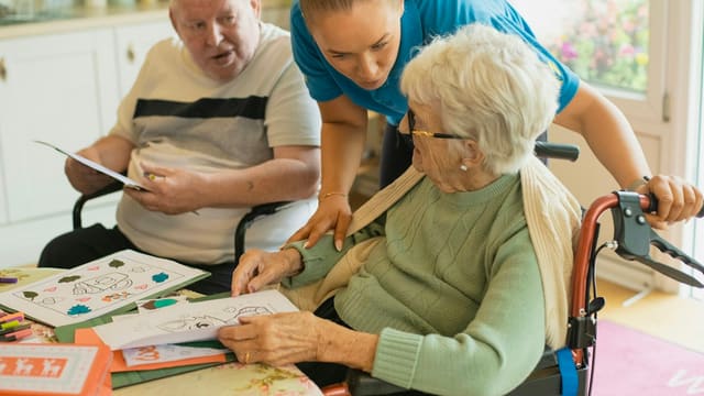 Caregiver assisting elderly couple with coloring