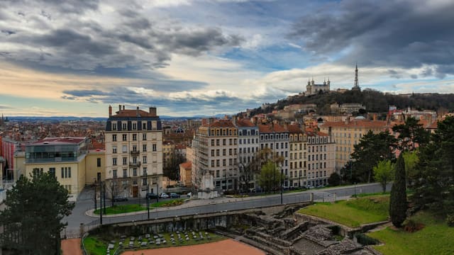 Les vestiges de l'amphithéâtre des Trois Gaules au pied des immeubles de la Croix-Rousse, avec la colline de Fourvière et sa basilique à l'horizon.