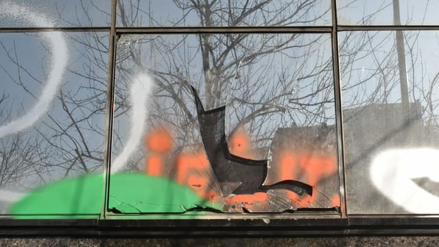 Vitrine brisée et taguée, aux éclats de verre éparpillés, illustrant les dégradations subies par les commerces pillés.
