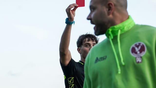 A man in a green hoodie holding up a red card