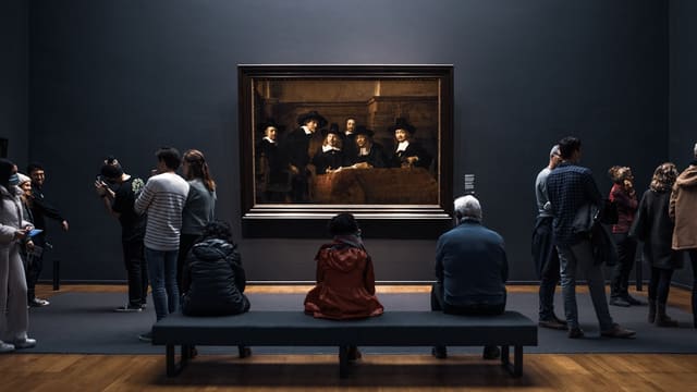a group of people standing around a museum looking at a painting