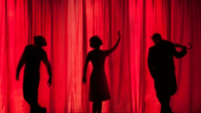 Trois silhouettes d'acteurs se détachent devant un rideau de scène rouge.