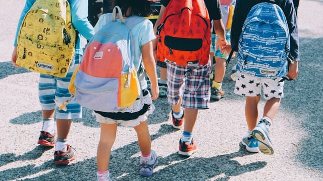 group of people wearing white and orange backpacks walking on gray concrete pavement during daytime