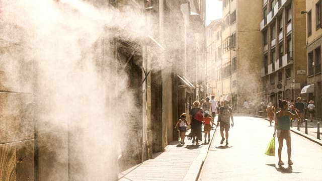 People walk down a sunny street with misting spray.
