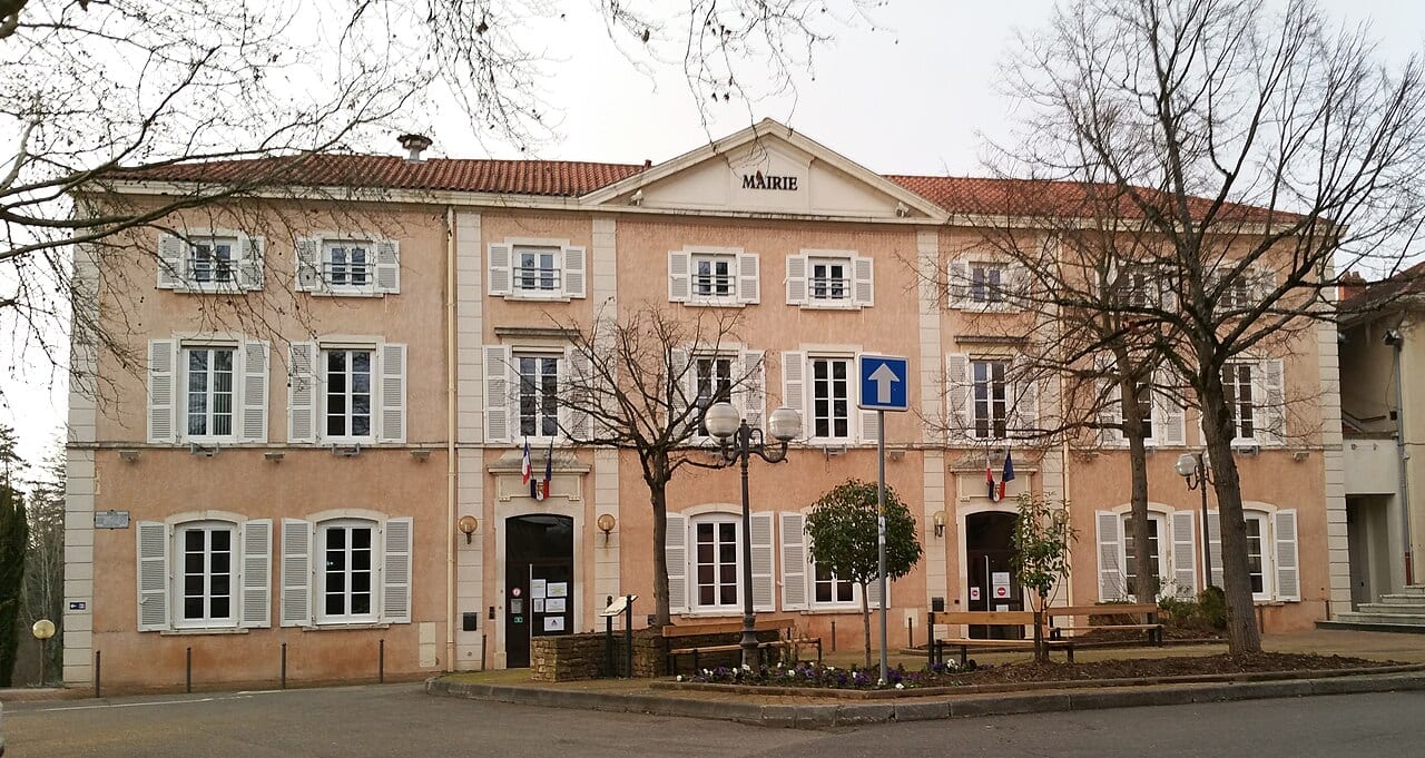 Façade de la mairie de Charbonnières-les-Bains, bâtiment rose à fronton et volets blancs, avec des arbres dénudés au premier plan.