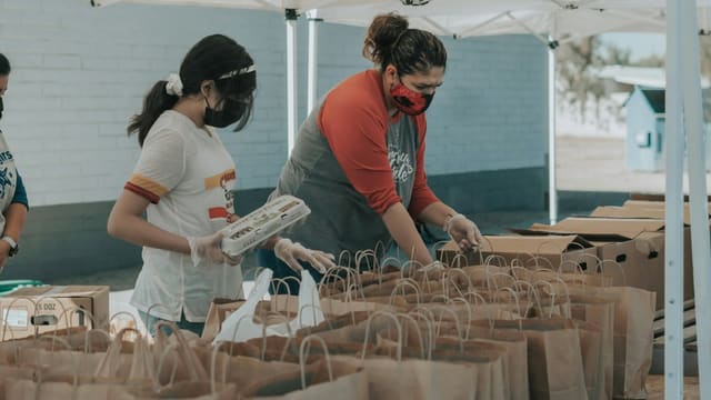 Des bénévoles masqués préparent des sacs de denrées alimentaires lors d'une collecte solidaire.