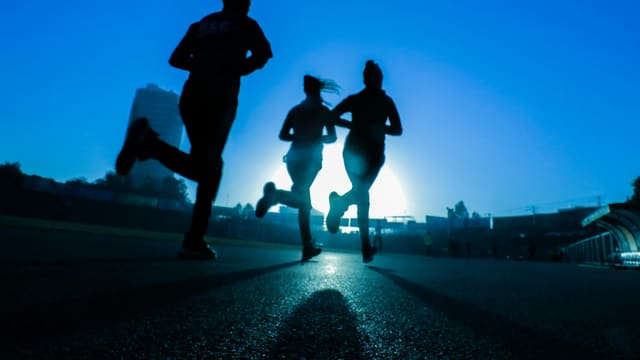silhouette of three women running on grey concrete road