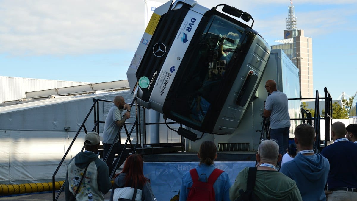 A group of people watching a Mercedes-Benz truck cab tilted vertically on a platform