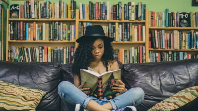 woman reading a book while sitting on black leather 3-seat couch