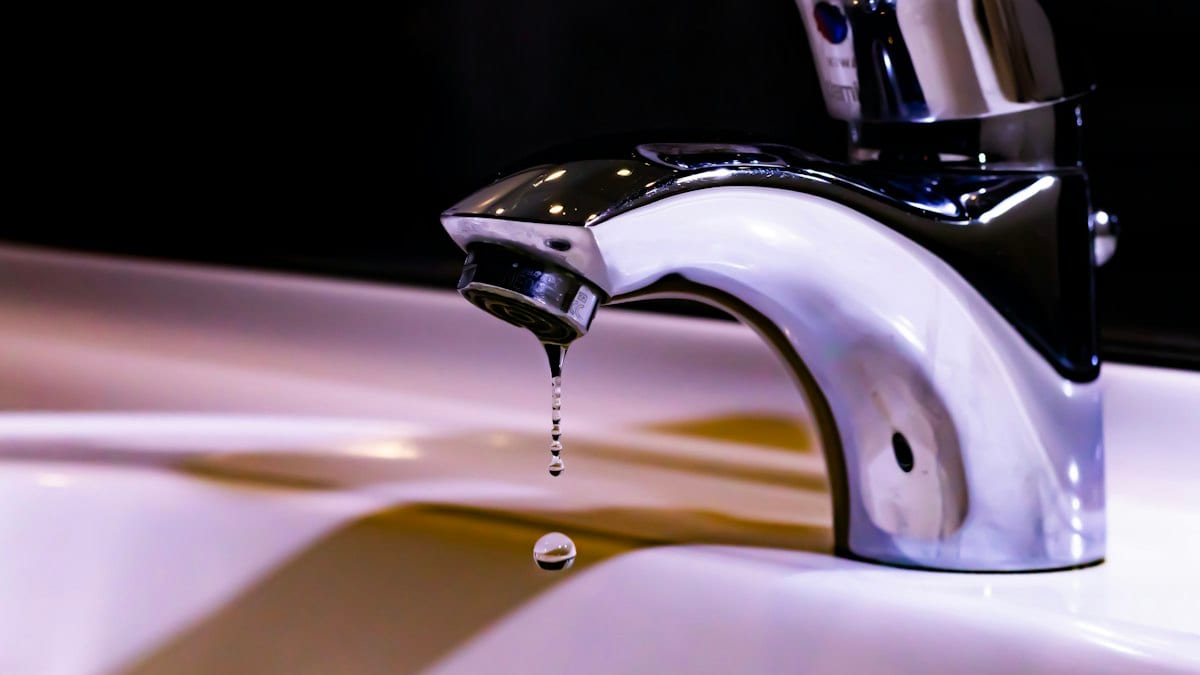 Goutte d'eau tombant d'un robinet chromé au-dessus d'un lavabo blanc.