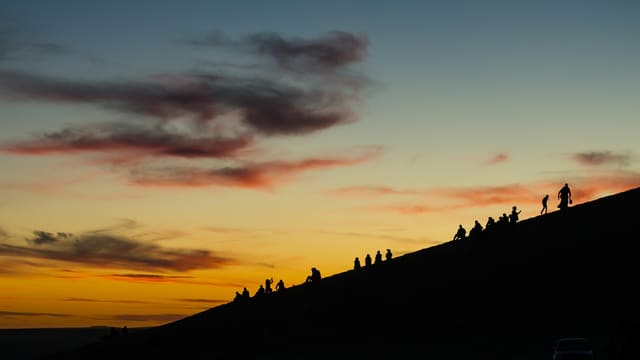Silhouettes de spectateurs rassemblés sur une colline face au soleil couchant
