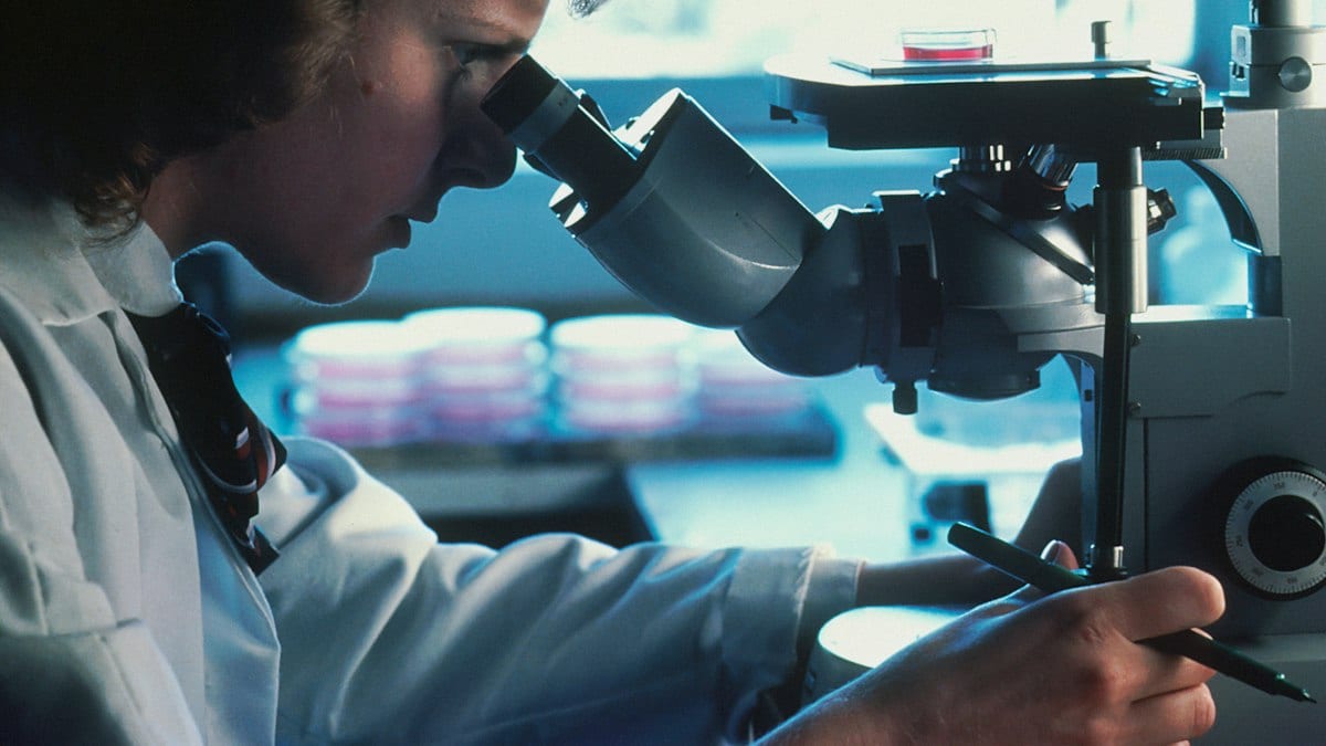 A person in a white lab coat looking through a microscope in a laboratory