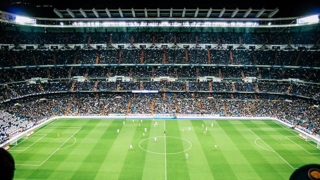Vue d'ensemble d'un grand stade de football éclairé de nuit, pelouse verte et tribunes pleines, pour illustrer un match européen.