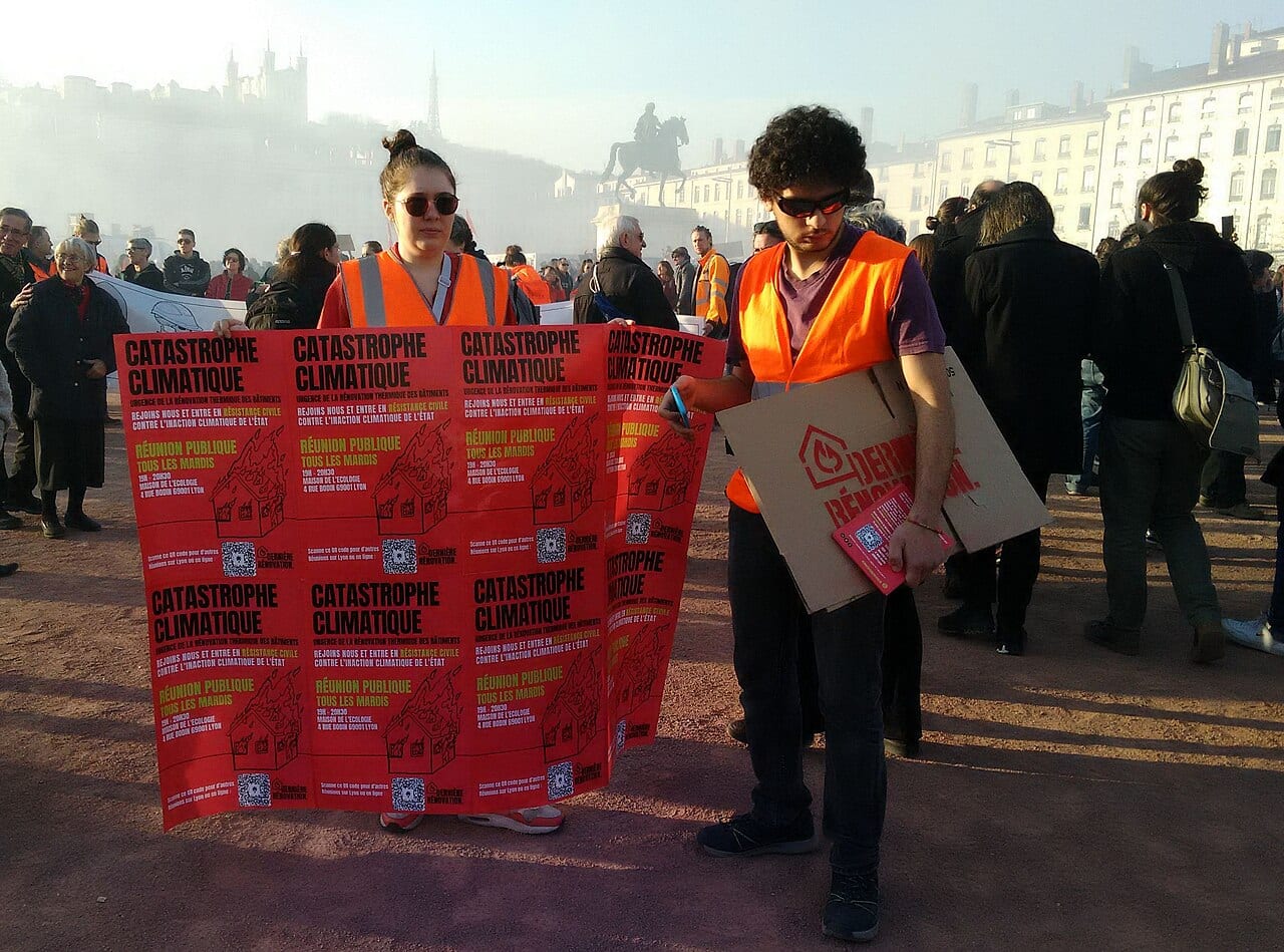 Fin de la manifestation place Bellecour, deux personnes avec des banderoles et pancartes sur l'urgence climatique et les réunions publiques chaque mardi à la maison de l'écologie. A l'arrière-plan, la