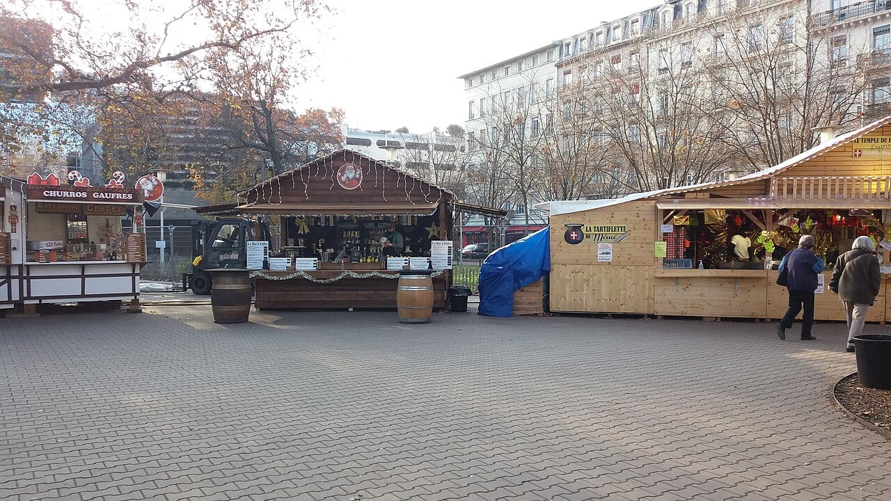 Chalets en bois d'un marché de Noël installé sur une place lyonnaise, avec passants.