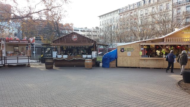 Chalets en bois d'un marché de Noël installé sur une place lyonnaise, avec passants.