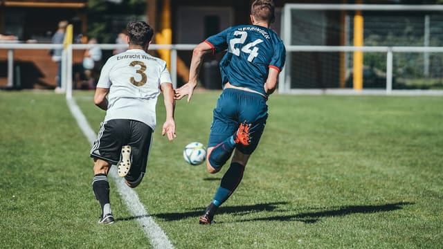 2 men playing soccer on green grass field during daytime