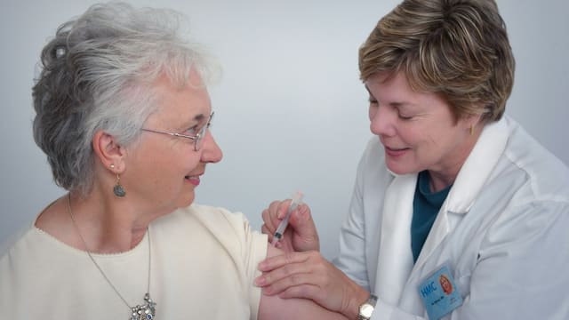 Une infirmière prépare une injection vaccinale dans le bras d'une patiente âgée.