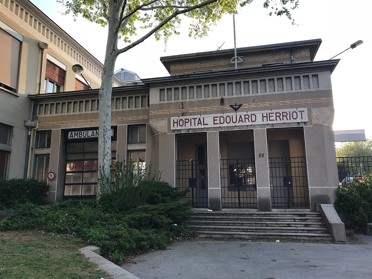 Entrée de l'hôpital Édouard Herriot à Lyon, bâtiment en pierre avec enseigne, escalier et accès des ambulances