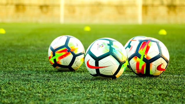 three white-and-black soccer balls on field
