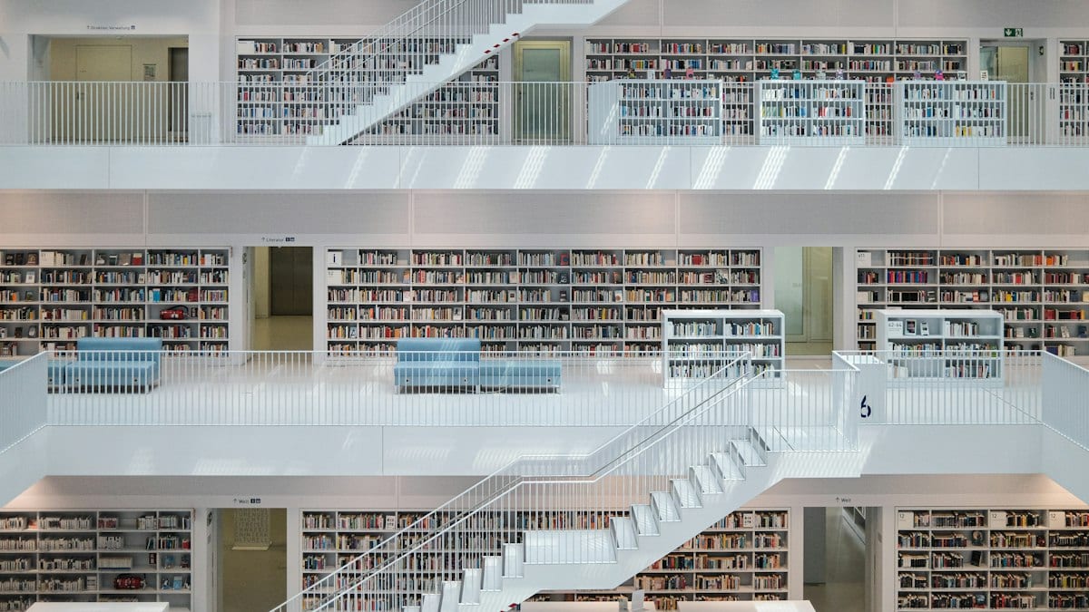 Une médiathèque moderne aux rayonnages de livres répartis sur plusieurs étages reliés par des escaliers clairs.