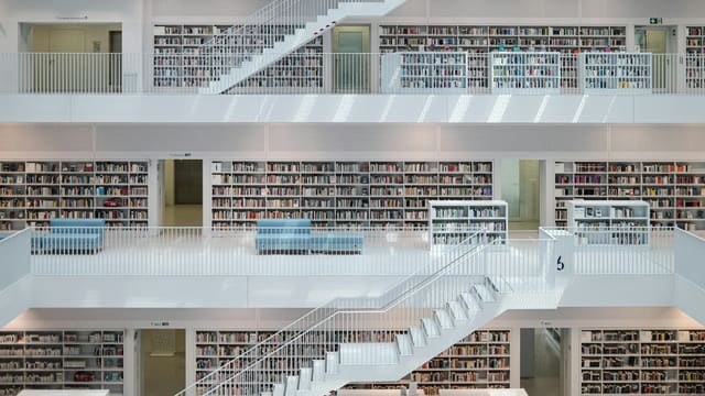 Une médiathèque moderne aux rayonnages de livres répartis sur plusieurs étages reliés par des escaliers clairs.