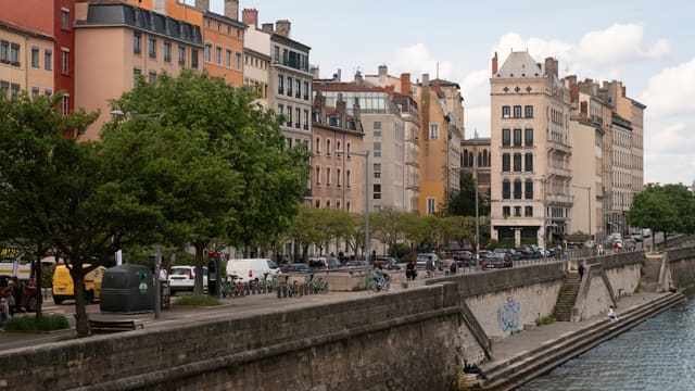 Buildings line a river with trees and a sidewalk.