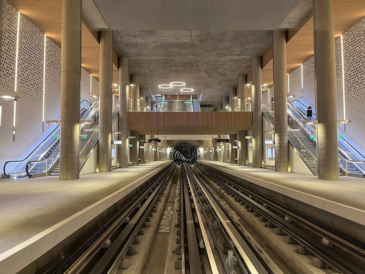 Quais et escalators d'une station de métro lyonnaise, vue depuis les voies, avec le tunnel au fond.