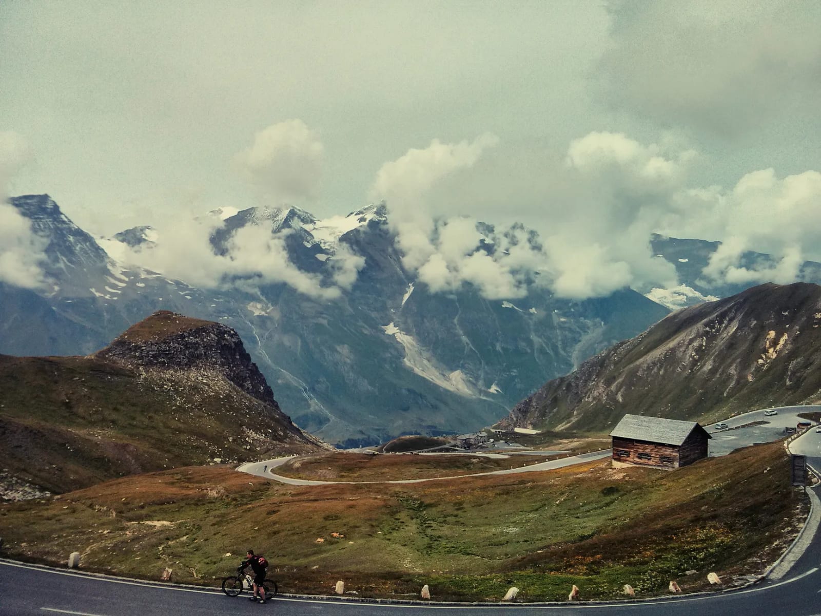 Route alpine sinueuse avec chalet et chaîne montagne.