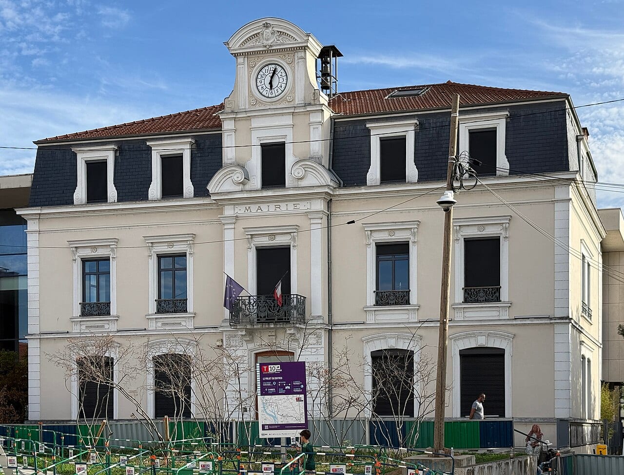 Façade de la mairie de Saint-Fons, avec son fronton orné et son horloge, sous un ciel dégagé.