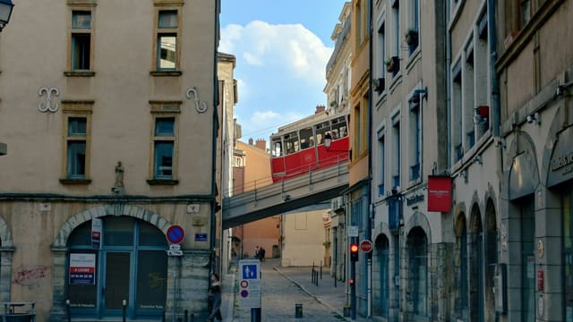 Narrow street with old buildings and an elevated red bridge.