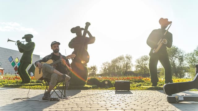 Musicians playing instruments outdoors with statues behind them