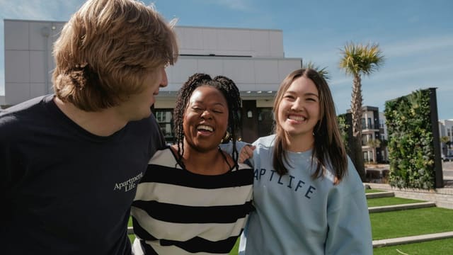 Three smiling friends stand together outdoors.