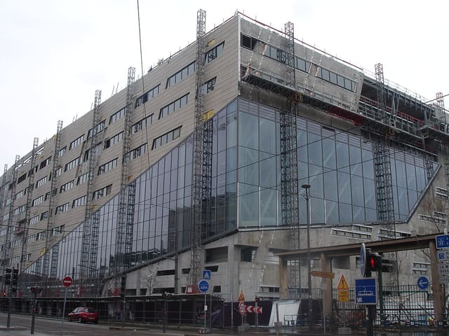Façade vitrée et métallique du siège de la Région Auvergne-Rhône-Alpes, encore en chantier, quai Rambaud à Lyon, avec échafaudages et tramway au premier plan.