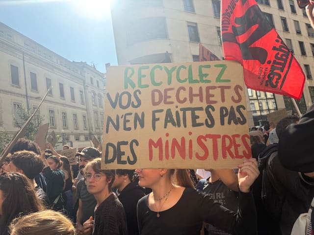 Une manifestante brandit une pancarte en carton : « Recyclez vos déchets, n'en faites pas des ministres »