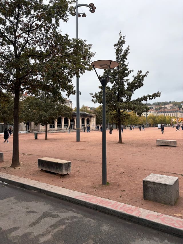 Sur la place Bellecour, à Lyon, le pavillon de l'office de tourisme incendié, aux arcades noircies et entouré de barrières, sous un ciel gris.