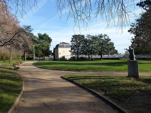 Allées et pelouses du jardin des Chartreux à Lyon, avec un pavillon au toit d'ardoise et la ville en arrière-plan