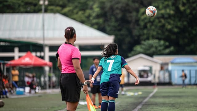 Une arbitre de football en maillot rose suit le jeu lors d'un match féminin.