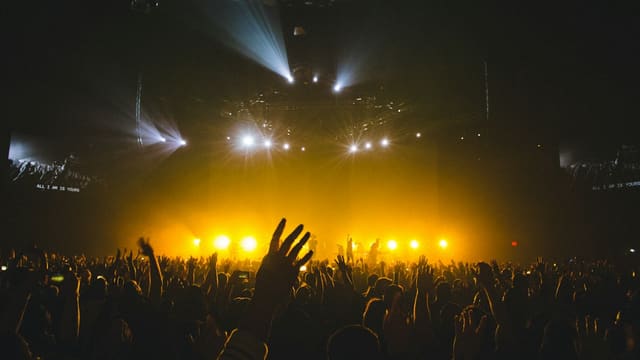 Foule levant les mains devant une scène baignée de lumière dorée, ambiance de concert.