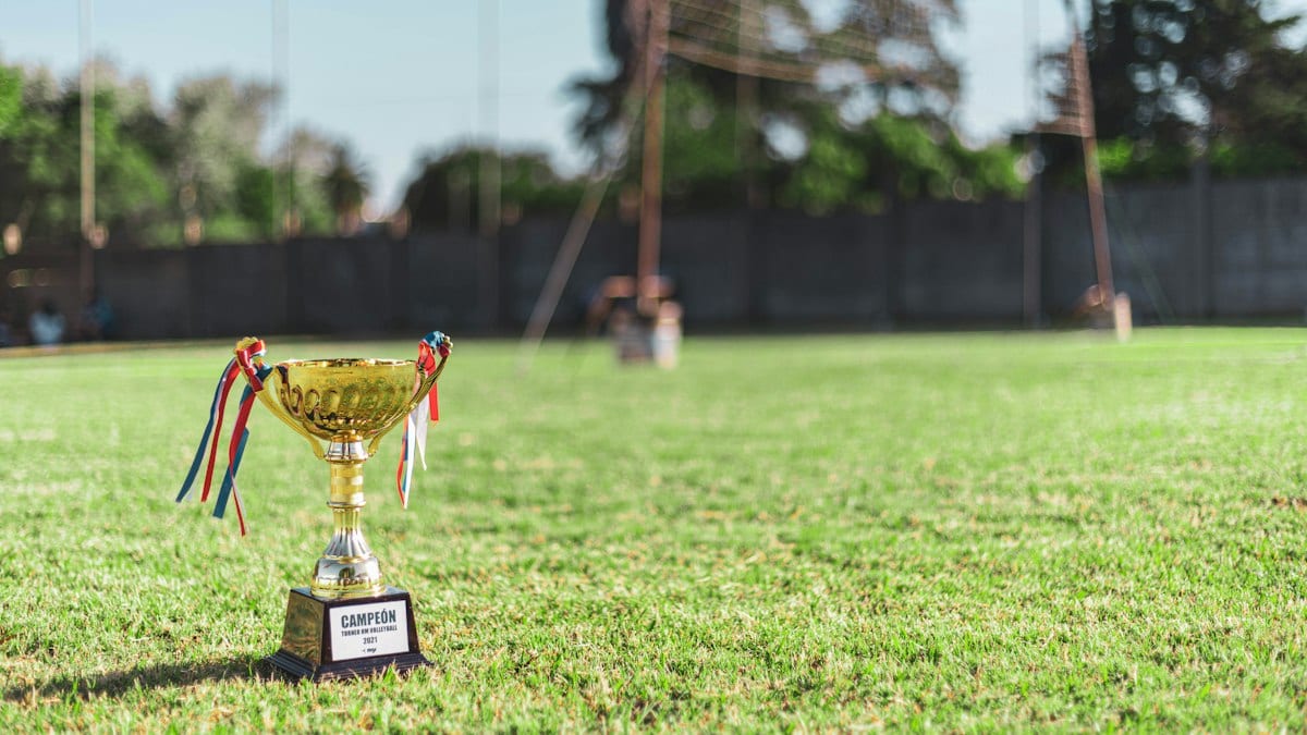 Trophée de champion posé sur un terrain de football, but en arrière-plan