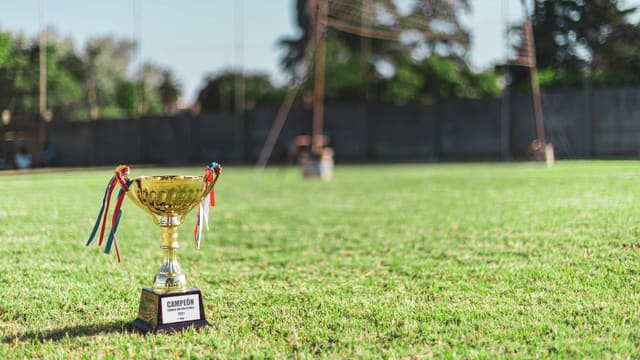 Trophée de champion posé sur un terrain de football, but en arrière-plan