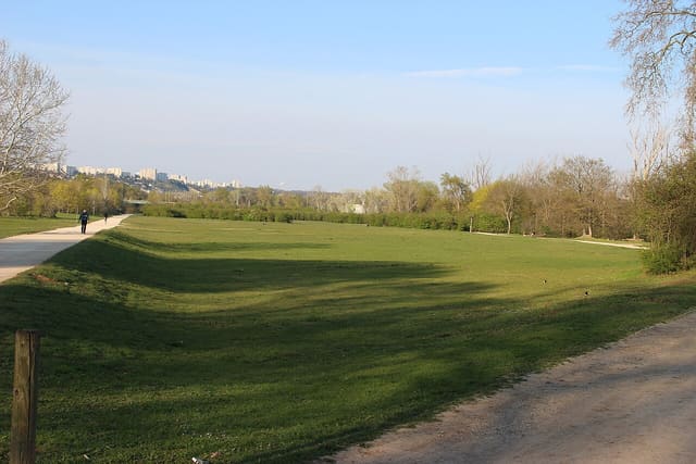 La grande plaine du parc de la Feyssine à Villeurbanne, traversée d'un chemin, avec la silhouette de Lyon à l'horizon.