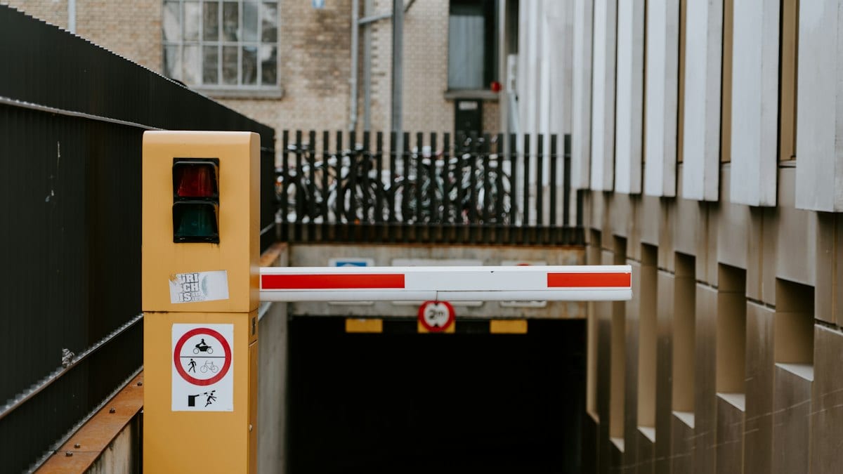 Barrière rouge et blanche levée à l'entrée d'un parking souterrain, avec sa borne jaune à feu tricolore.