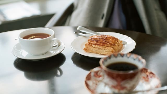 bread on ceramic plate near white ceramic teacup filled with coffee